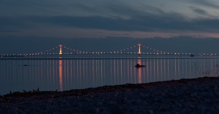 The Mackinac Bridge at twilight with colored lights that are reflecting in the water.