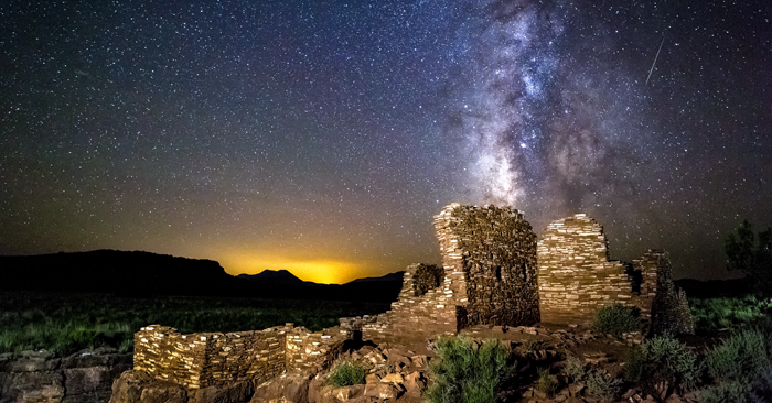 The Milky Way sets over Lomaki Puelbo at Wupatki National Monument, with the glow of Flagstaff in the distance. Photo by Flickr user CEBImagery, licensed under CC BY-NC 2.0.