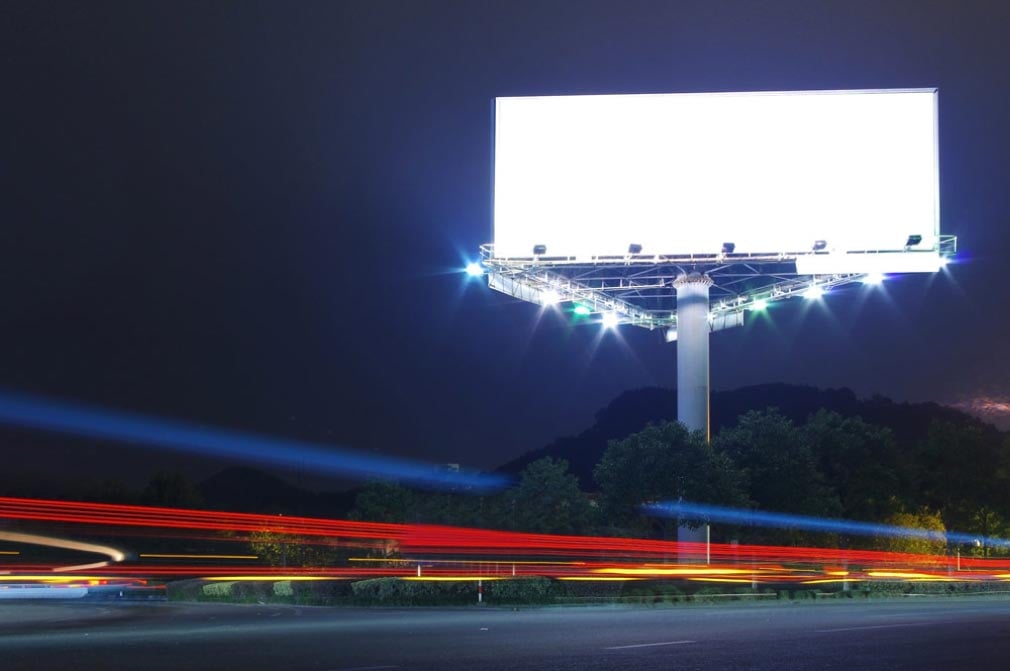 Picture of an extremely bright billboard over a roadway at night.