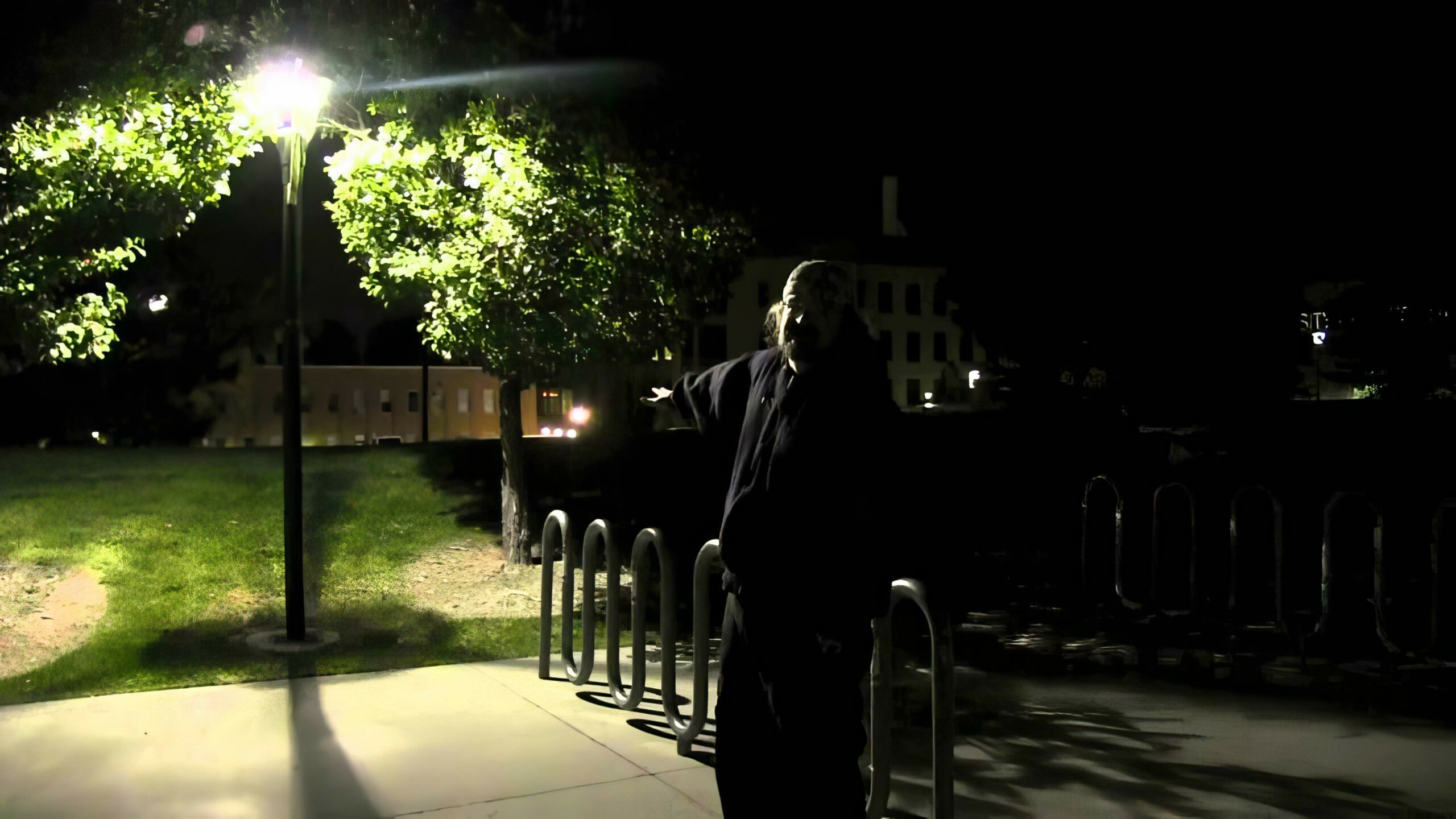 A man at night, nearly hidden in the glare of a park light.